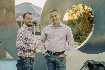 Dva muži před sochou, symbol spolupráce a přátelství.